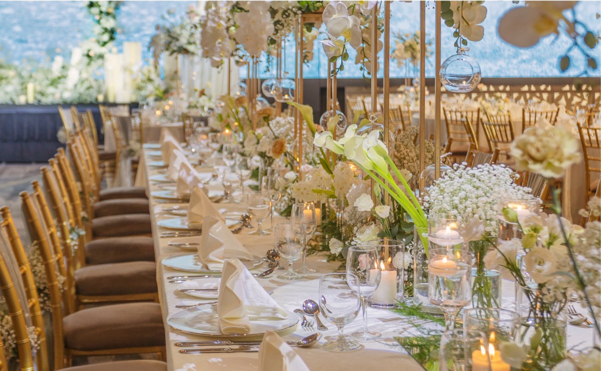 An elegantly set banquet table adorned with white flowers and candles, creating a festive atmosphere suggestive of a wedding or formal event.